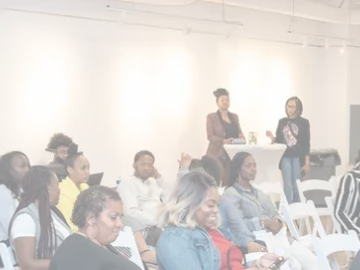 Audience seated at a conference, listening to speakers at the front of the room.