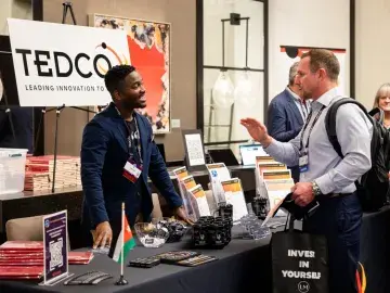 TEDCO 2025 Entrepreneur Expo; Sam Shoge, RUBII mentor, talking with attendee at the TEDCO exhibit table
