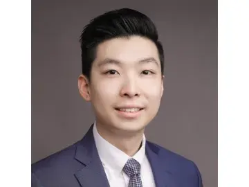 Chung Hei Sing smiling man in a navy suit against a gray background