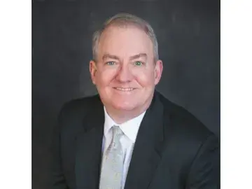 Cliff Coppersmith in dark suit and tie against gray background.