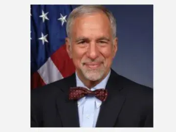 Phillip Singerman in suit and bow tie, U.S. flag behind him