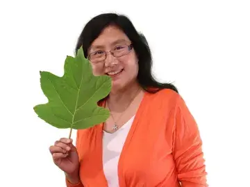 Julia Deng in orange cardigan holding a large green leaf on white background.