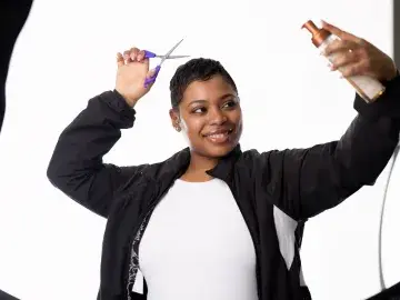 DeJonna Farrar holding scissors and hairspray pretending to cut her hair.