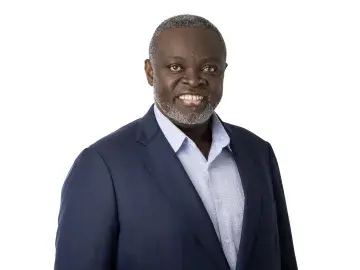 Benga Erinle in navy suit and light blue shirt, studio portrait on white background.