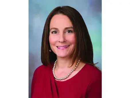 Ann Liebschutz in a red top with a pearl necklace, smiling.