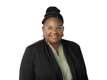 Rajaniece Thompson smiling in glasses, black blazer, on white background.