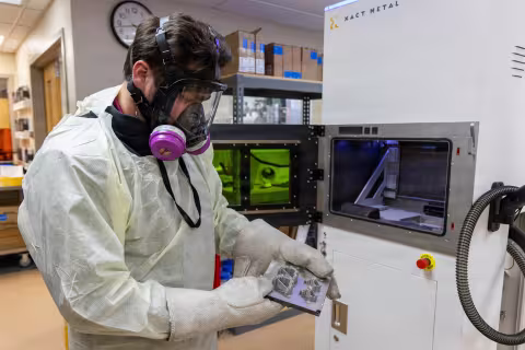 Lab worker in protective suit and respirator operating a 3D printer in a lab