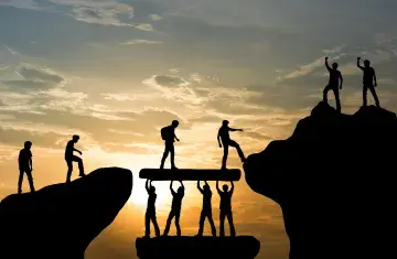 Silhouettes of hikers bridging a cliff gap at sunset.