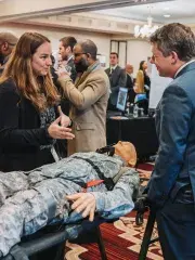 Conference networking scene with a person in camouflage lying on a massage table in foreground