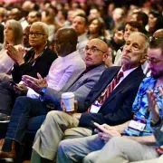 Front-row conference attendees seated and applauding in a crowded auditorium